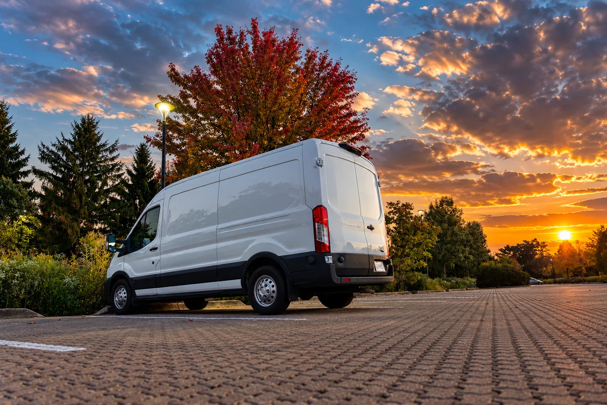 White Ford Transit van parked beneath autumn trees at sunset